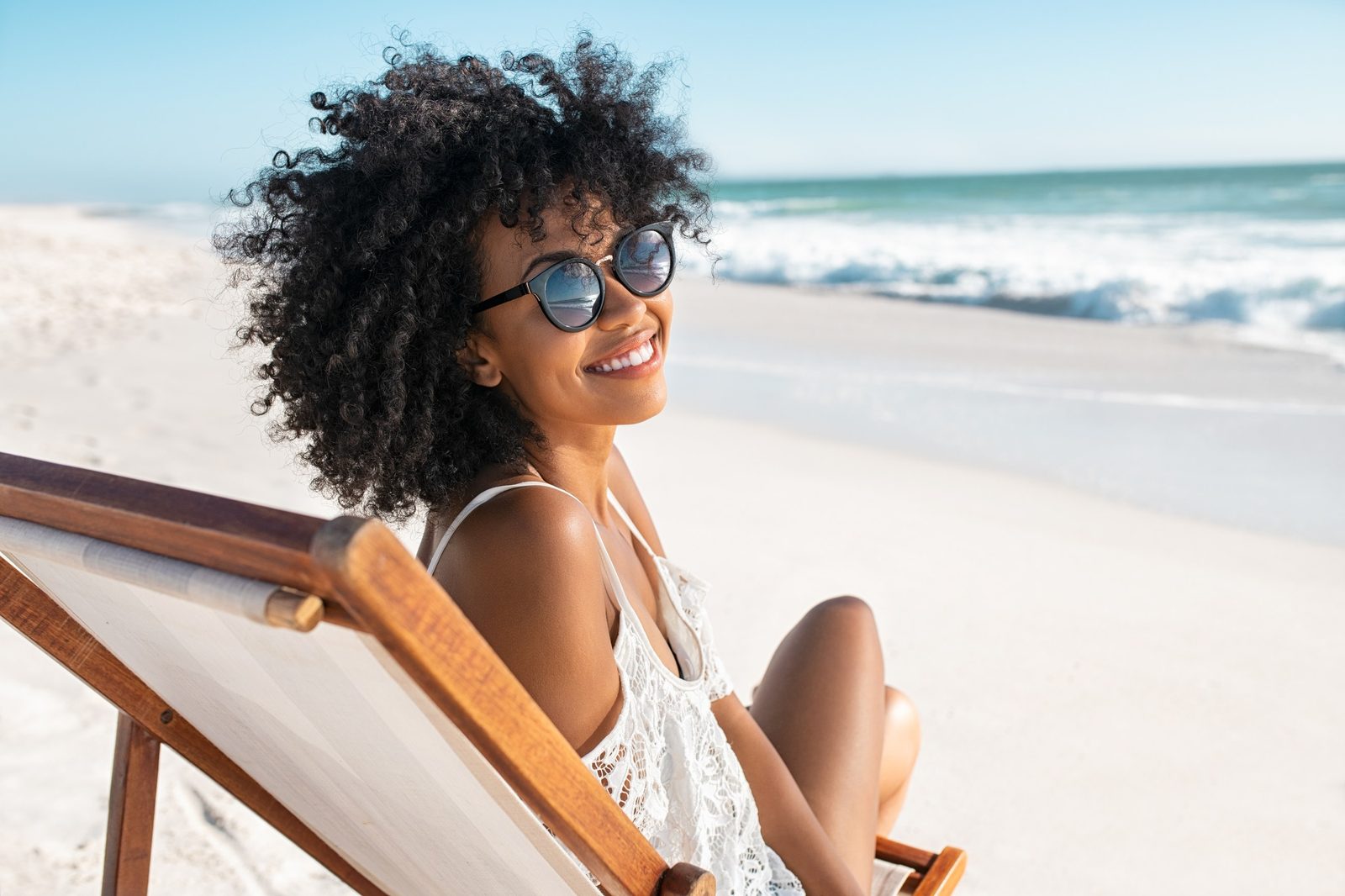 A woman smiling on a beach in sunglasses