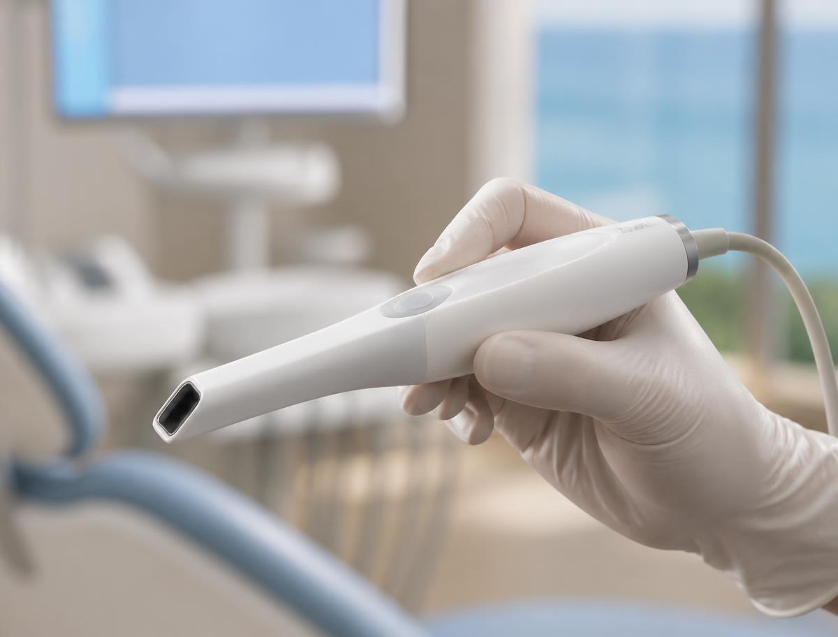 Gloved hand holding a modern intraoral camera wand in a bright dental treatment room